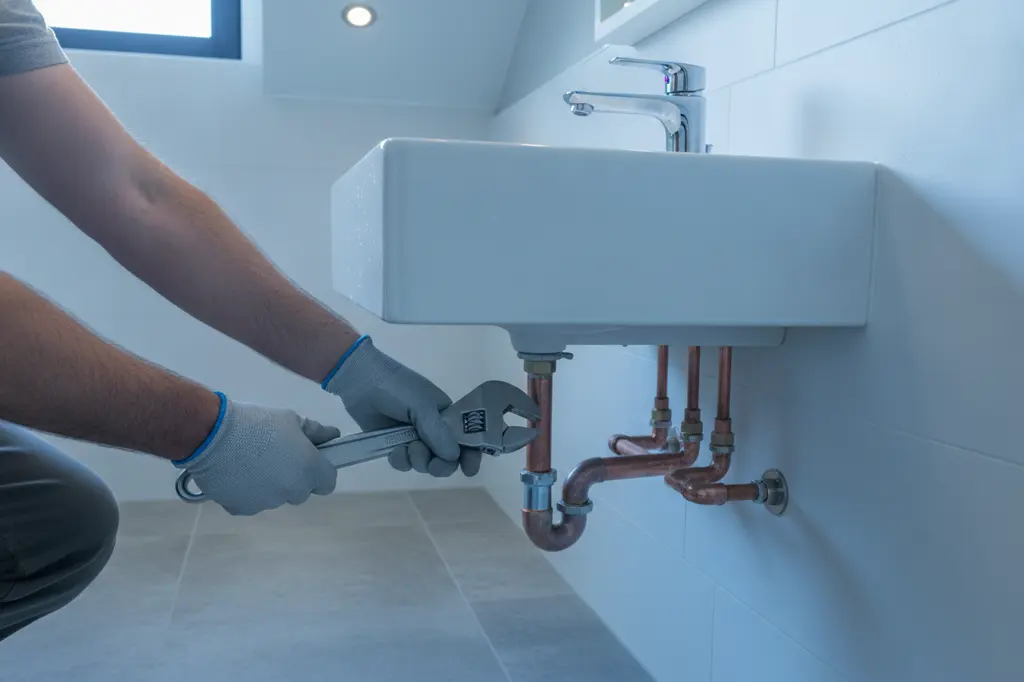 Plumber tightening copper supply lines under a wall-mounted bathroom sink